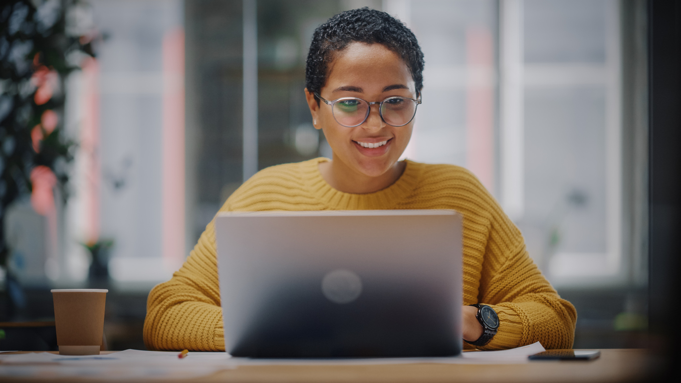 Smiling lady in glasses working on a laptop computer working on connecting to VPN, a common it helpdesk issue