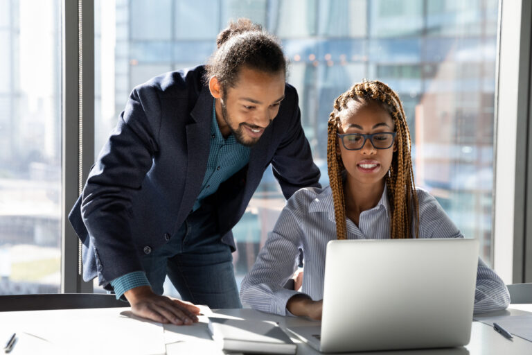 Smiling multiethnic colleagues work on laptop together to handle IT challenges