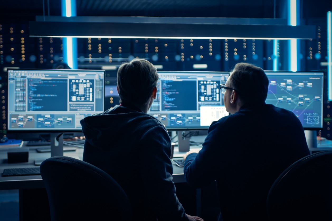 Scattered Spider attack monitoring - Two male IT professionals using computers to monitor a business's cybersecurity defenses.