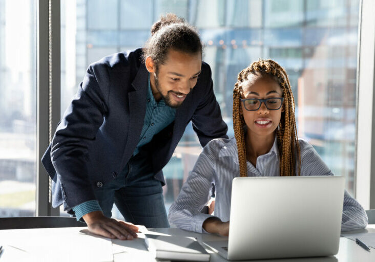 Smiling multiethnic colleagues work on laptop together to handle IT challenges